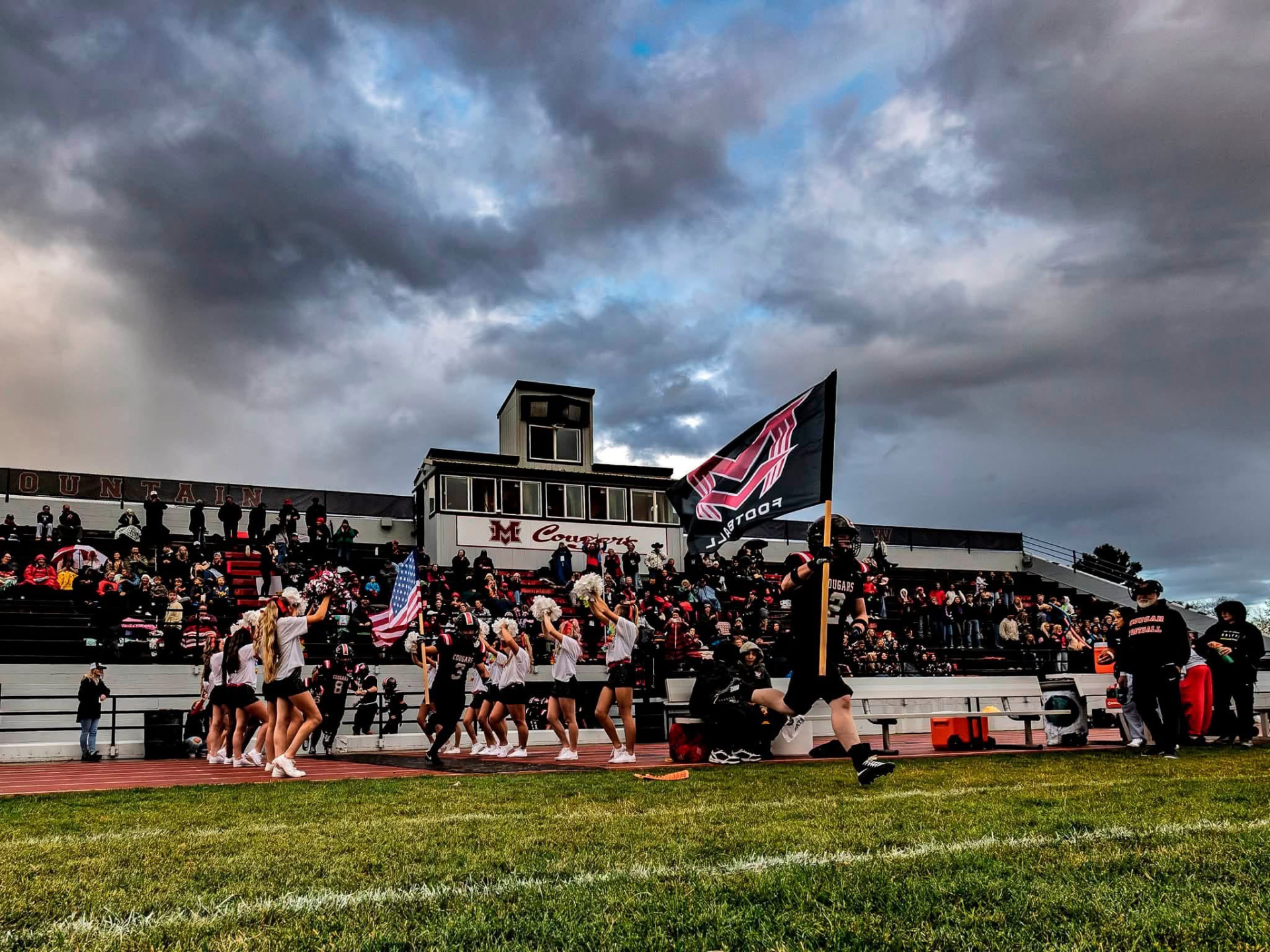 Cougars player runs onto the field carrying a flag past cheerleaders and the crowd